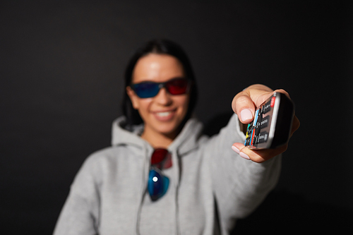 Portrait of young woman switching on the TV and watching movie in 3D glasses over black background