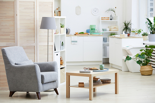 Image of armchair and wooden table in the living room with modern kitchen in the background