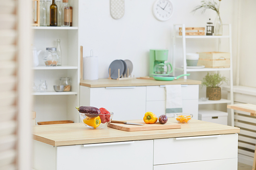 Image of kitchen table with wooden cutting board and fresh vegetables on it in the kitchen