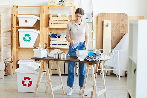 Young woman standing at the table and recycling the waste into the plastic containers in warehouse