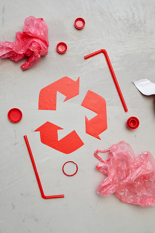 Close-up of red recycling symbol with garbage around it isolated on grey background