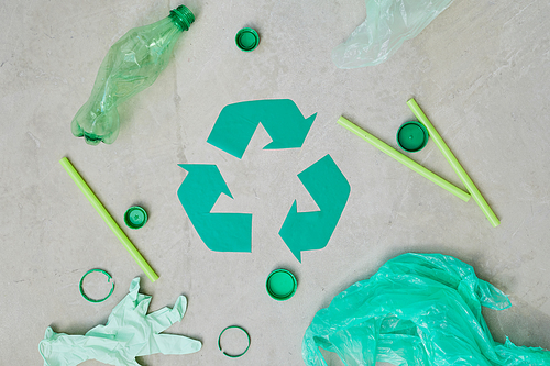 Close-up of green recycling symbol with plastic bottles and bags isolated on grey background
