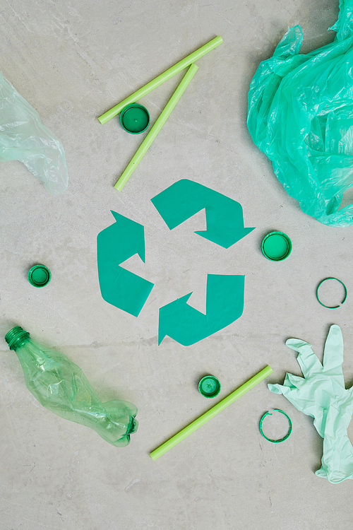 Close-up of green recycling symbol with garbage around it isolated on grey background