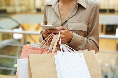 Close-up of woman holding shopping bags and using her mobile phone while standing in shopping mall