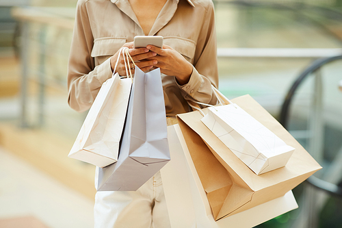 Close-up of young woman holding paper bags and communicating online on her mobile phone during shopping in the store