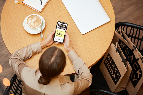 High angle view of young woman sitting at the table with shopping bags and using her mobile phone in cafe