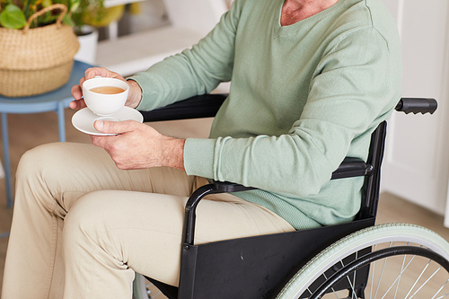 Close-up of disabled man sitting in wheelchair with cup of tea at home
