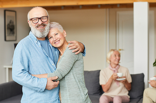 Portrait of happy senior couple standing embracing each other and smiling at camera at home