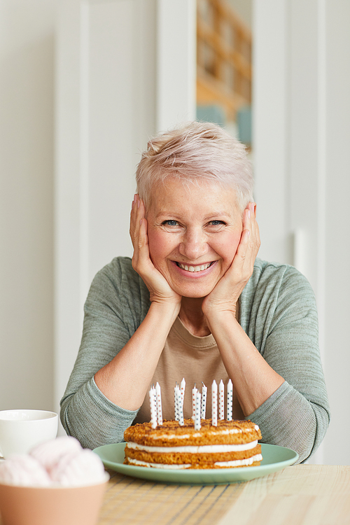 Portrait of happy senior woman sitting at the table with cake with candles and smiling at camera