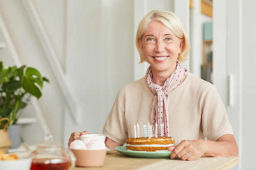 Portrait of senior blonde hair smiling at camera while sitting at the table with tea and cake