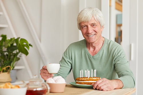 Portrait of senior man smiling at camera while sitting at the table with tea and birthday cake