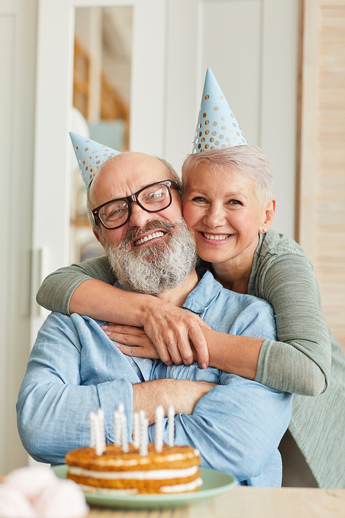 Portrait of happy senior family of two smiling at camera while sitting at the table with cake and celebrating birthday