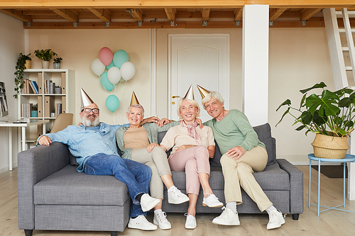 Portrait of group of senior people in party hats sitting on sofa and smiling at camera they celebrating birthday
