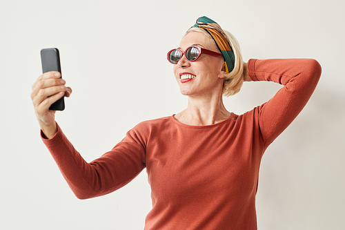Mature woman in sunglasses making selfie on her mobile phone against the white background