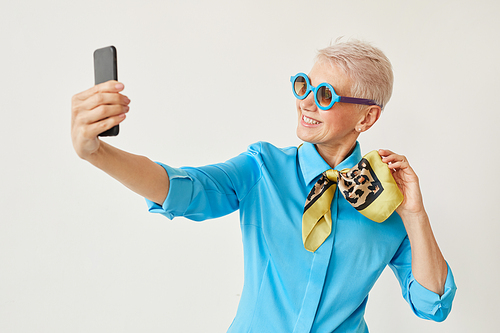 Senior elegant woman in sunglasses posing at camera on her mobile phone against the white background