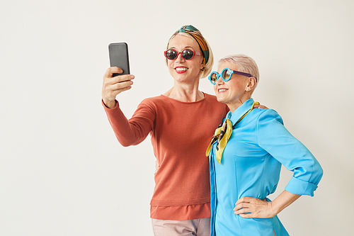 Two senior women in sunglasses making selfie on mobile phone against the white background