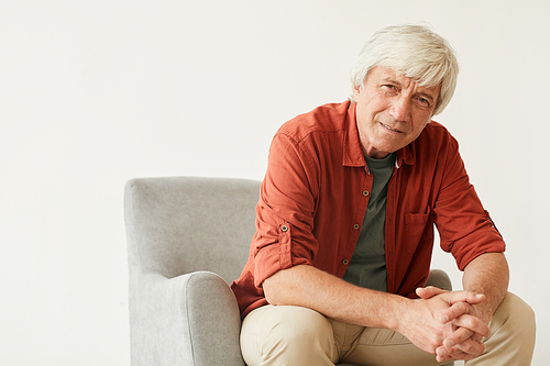 Portrait of mature man in casual clothing sitting on armchair against the white background