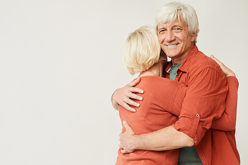 Portrait of mature man embracing his wife and smiling at camera against the white background