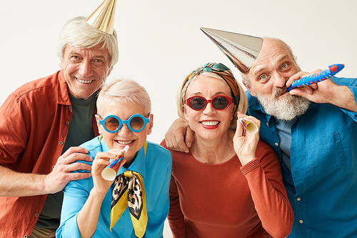 Portrait of senior people in party hats and sunglasses smiling at camera and having fun against the white background