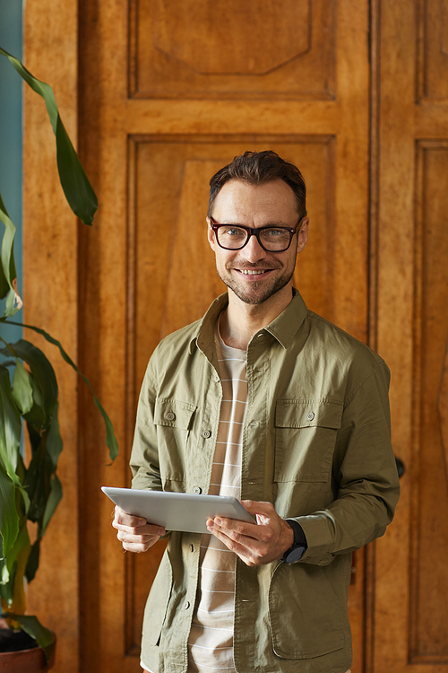 Portrait of mature man in eyeglasses smiling at camera while using digital tablet