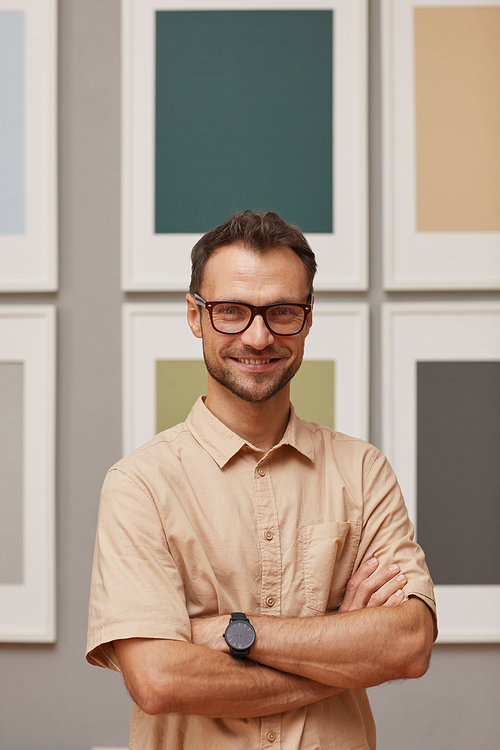 Portrait of young modern designer in eyeglasses standing with arms crossed and smiling at camera