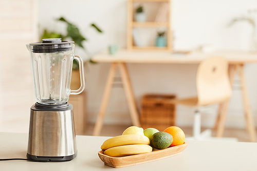 Image of fresh fruits prepared for cocktail with blender standing on the table in the kitchen