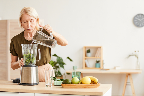 Mature woman sitting on a diet and she preparing a healthy cocktail in the morning in her kitchen