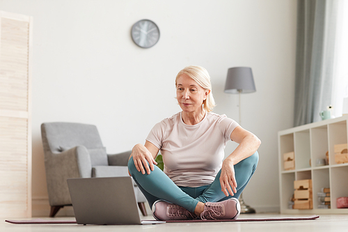 Senior woman sitting on the floor and looking at monitor of laptop she preparing for the sport exercises