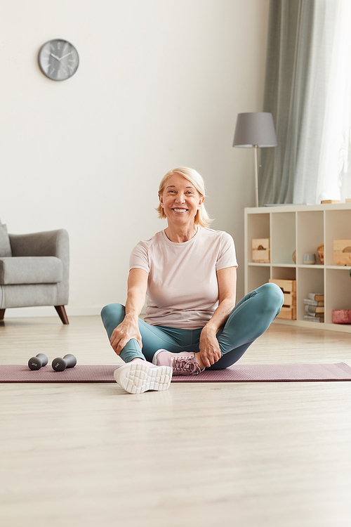 Portrait of happy mature woman sitting on the floor and resting after sports training at home she smiling at camera