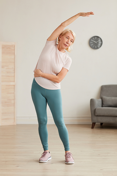 Senior woman standing and doing morning exercises in the room at home