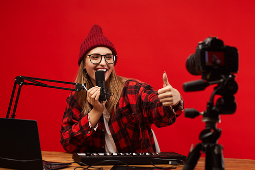 Young smiling woman in eyeglasses showing thumb up to the camera and singing she shooting the content