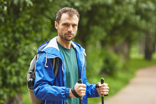 Portrait of young man holding sticks for sport walking and looking at camera standing in the forest
