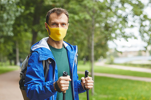 Portrait of young man in protective mask looking at camera while walking in the park