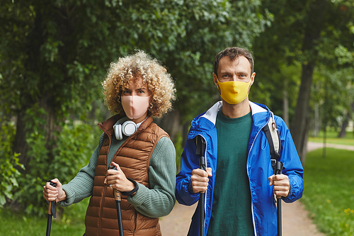 Portrait of young couple in protective masks looking at camera while doing sport walking during pandemic in the forest