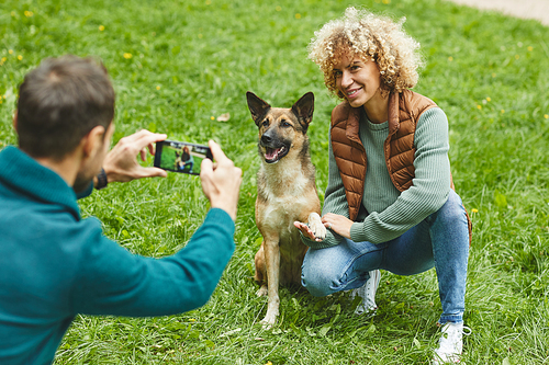 Young man making photo on his mobile phone of young woman and their pet outdoors