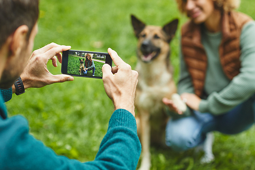 Rear view of man making photo on his mobile phone of his girlfriend and dog in the park