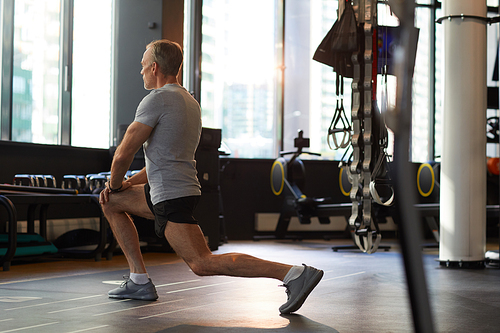 Rear view of mature man doing stretching exercises before sports training in gym