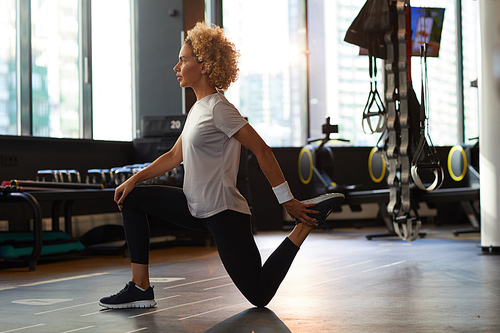 Side view of young woman warming up before sports training in gym