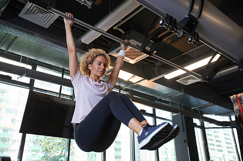 Young beautiful woman pulling up on horizontal bar she warming up before training in gym