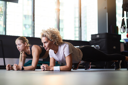 Two beautiful women exercising together on the floor during sports training in gym