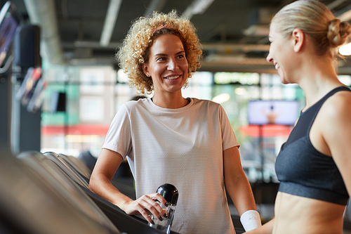 Smiling mature woman drinking water and talking to her friend they meeting in the gym