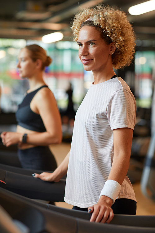 Mature beautiful woman training on treadmill in the gym with other people in the background