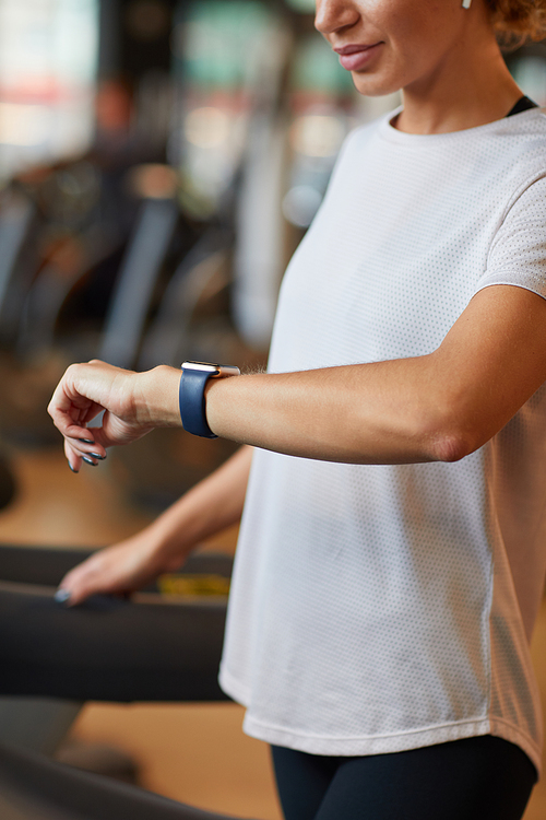 Close-up of healthy woman looking at watch on her arm and checking her pulse while training on treadmill in gym