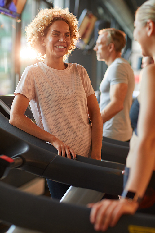 Happy beautiful woman talking to her friend during their sports training in gym