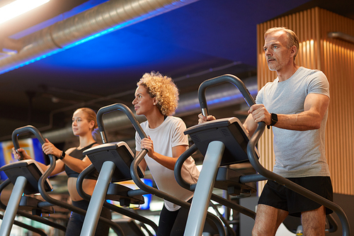 Group of people running together on treadmills during sports training in gym