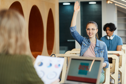 Content confident smart student girl in glasses raising hand to ask teacher at class in business school