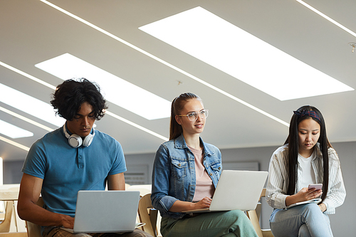 Group of young multi-ethnic students sitting with devices in row at university lecture