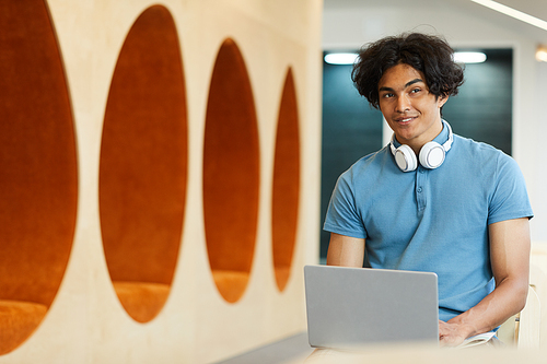 Smiling mixed race student with messy hair sitting in auditorium and typing lecture note on laptop