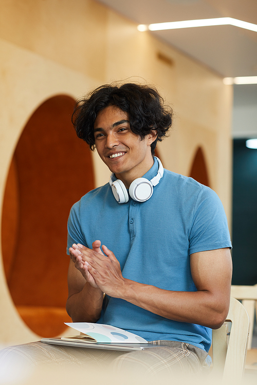 Positive handsome mixed race student with wireless headphones around neck clapping hands while admiring university teacher