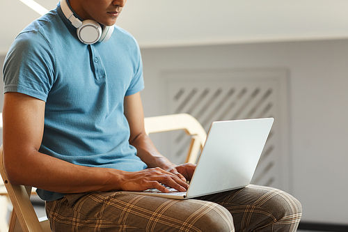 Close-up of serious mixed race student guy sitting on chair and using laptop while searching for information on internet